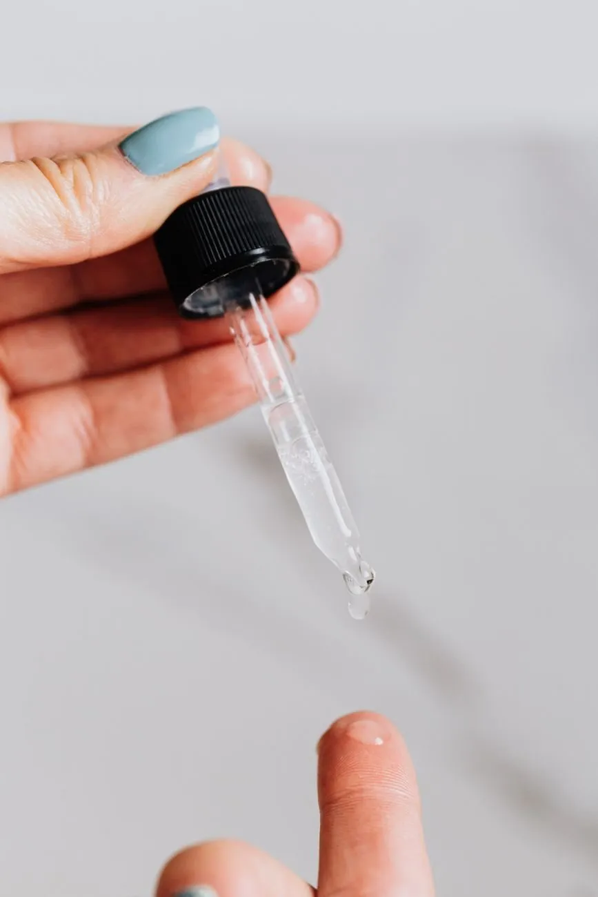 A hand holding a glass dropper over a fingertip, a single drop forming at the tip
