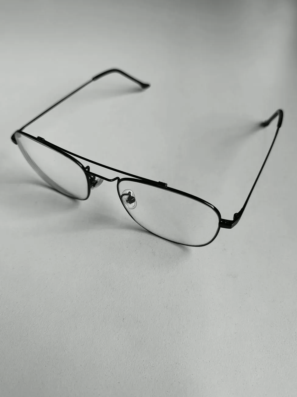 Thin black metal pilot glasses with a double bridge on a grey surface