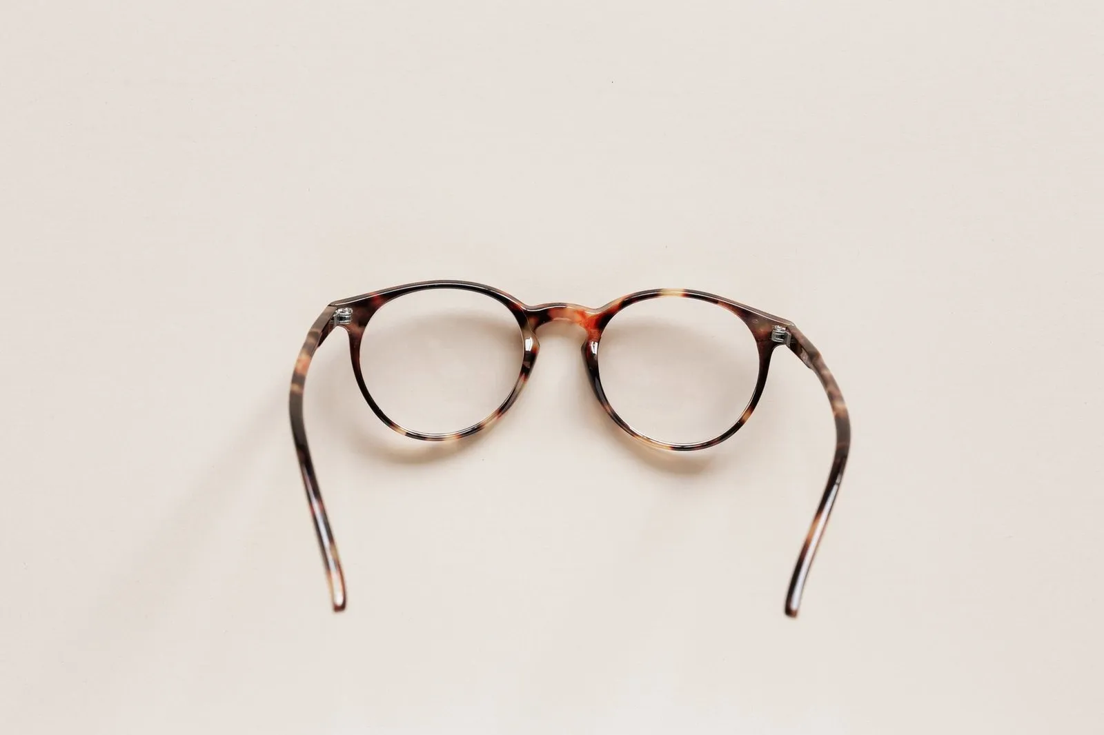 Round tortoiseshell glasses seen from behind on a cream surface