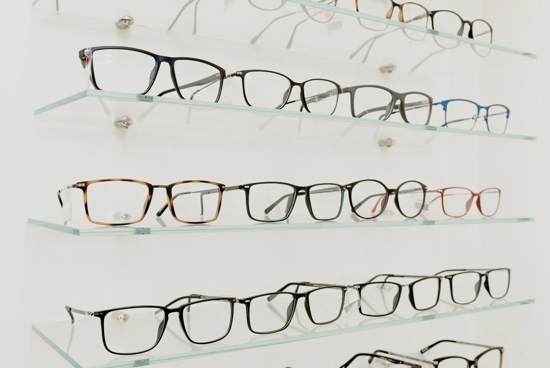 Rows of glasses on glass shelves against a white wall