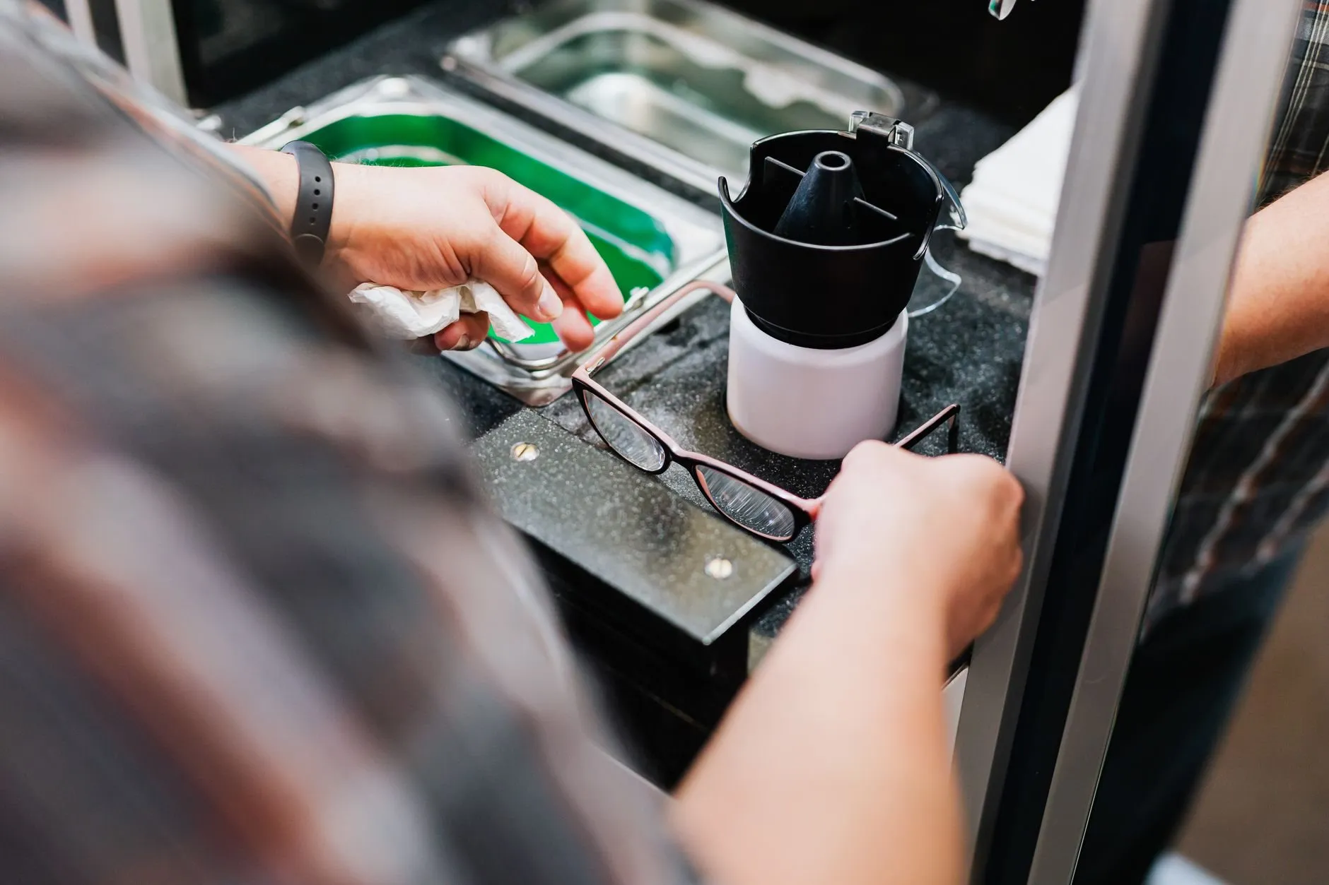 A dispensing optician's hands cleaning a pair of glasses at the workshop bench